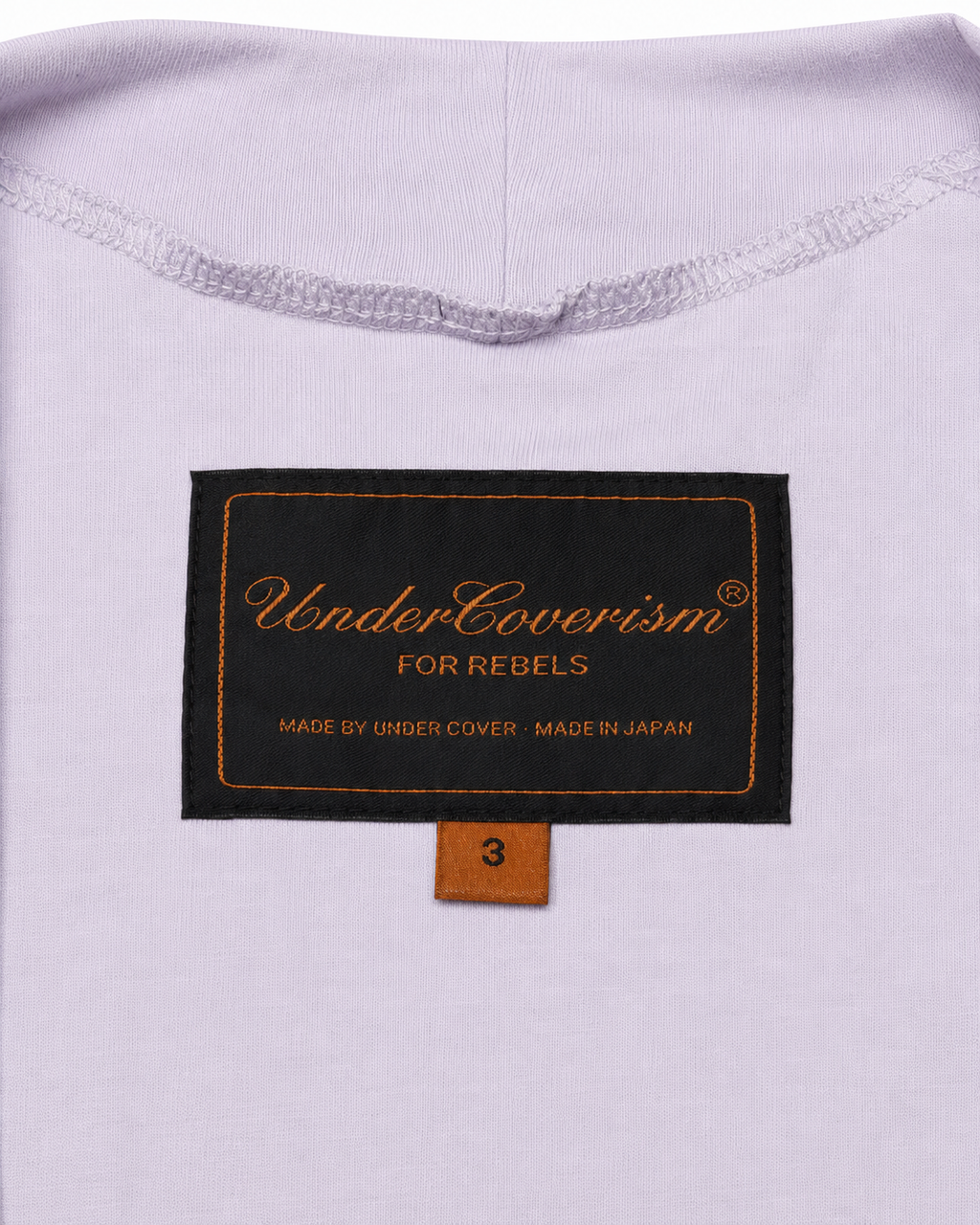 Close-up of a label on a light purple garment with text 'UnderCoverism For Rebels' and 'Made by Under Cover, Made in Japan'.