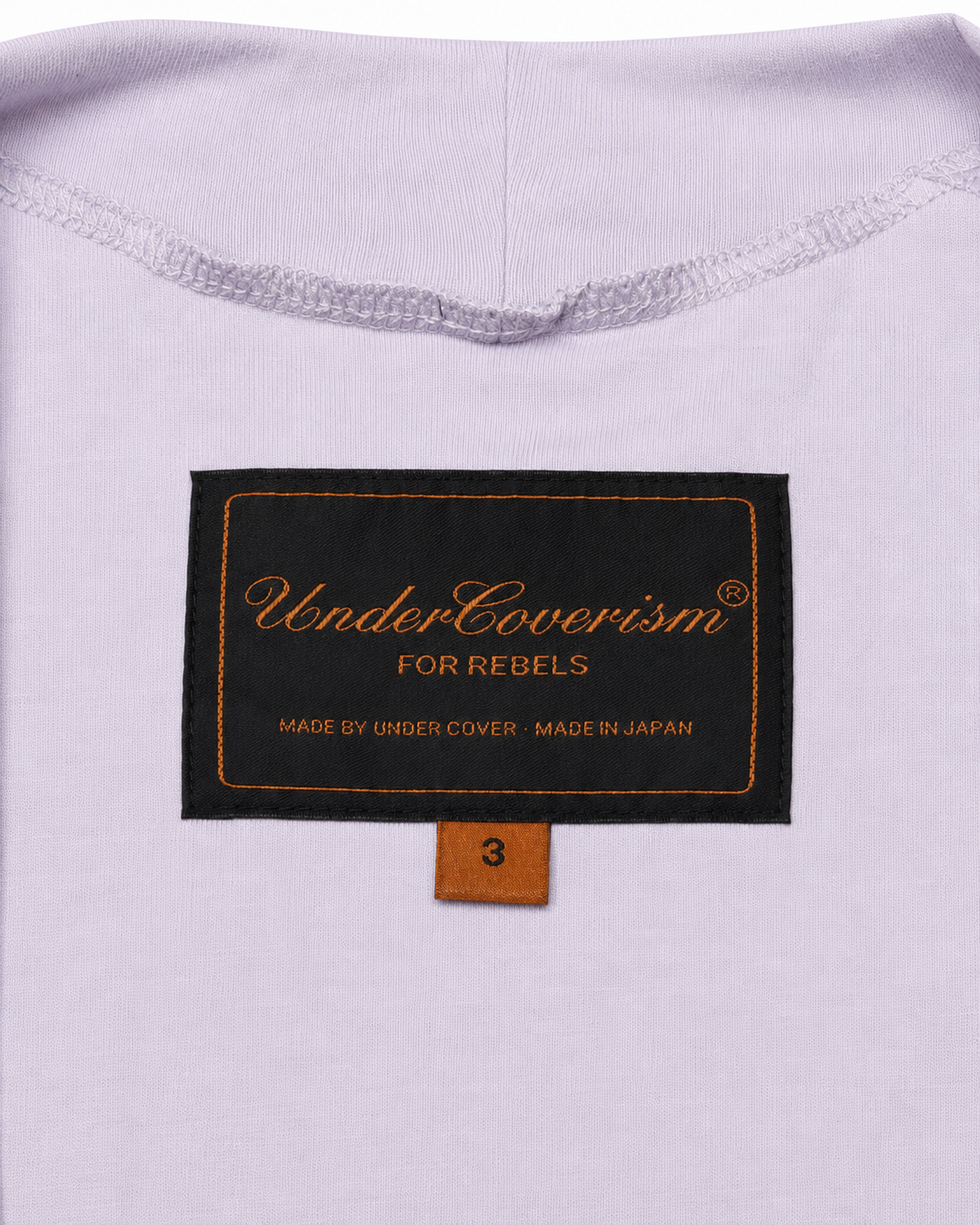 Close-up of a label on a light purple garment with text 'UnderCoverism For Rebels' and 'Made by Under Cover, Made in Japan'.