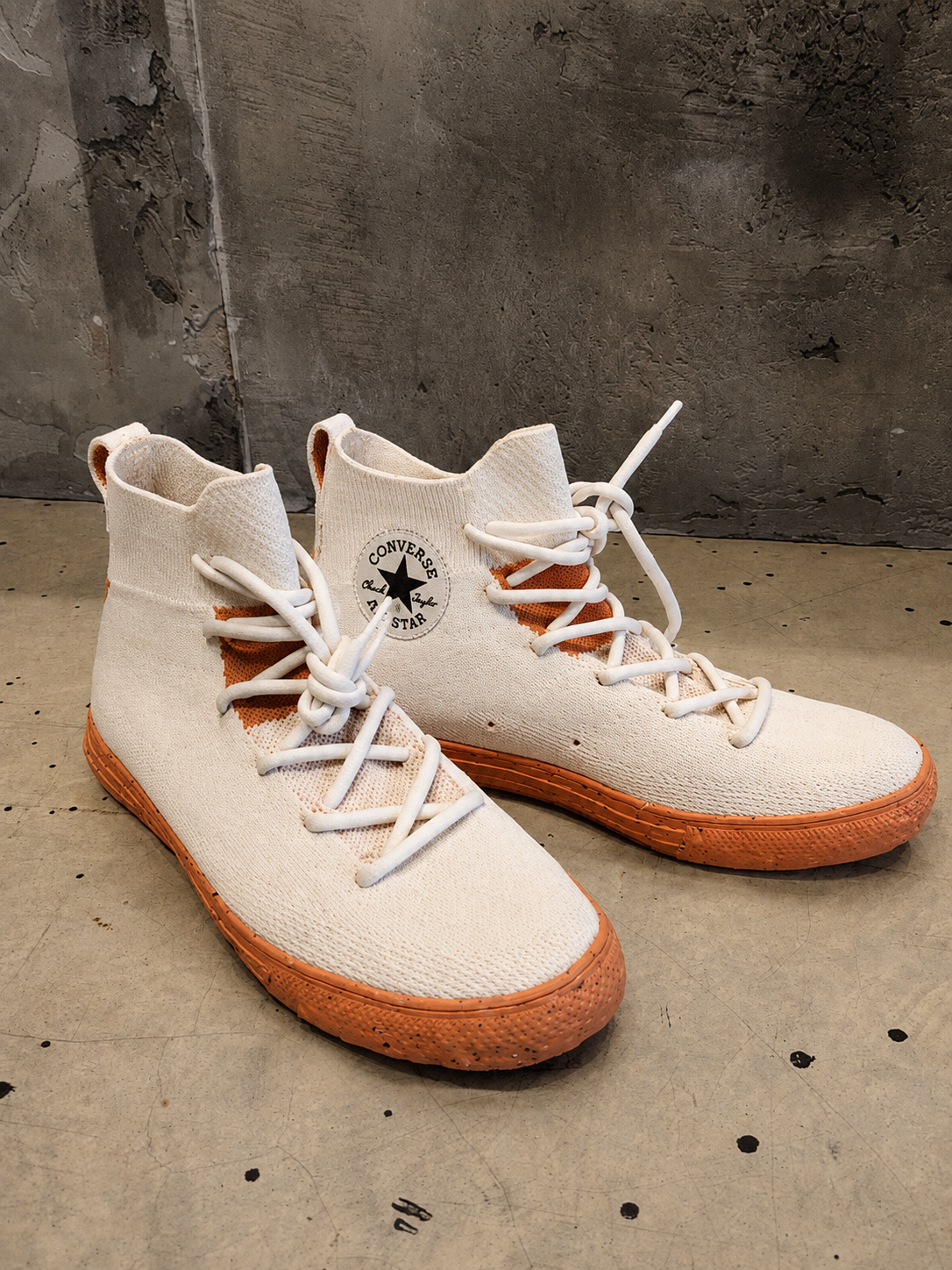 Pair of high-top sneakers with white laces and brown soles on a concrete floor.