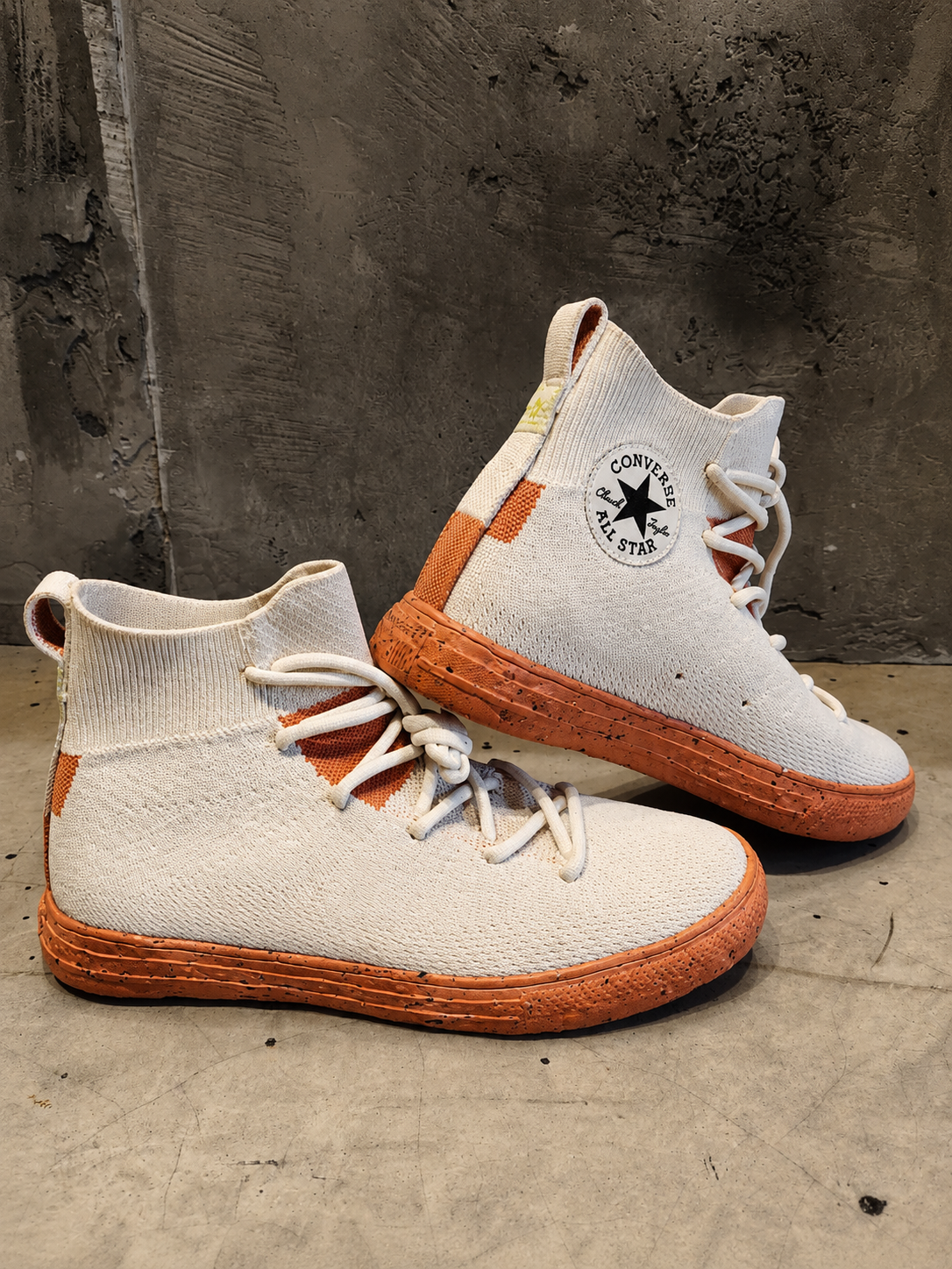 Pair of white and brown high-top sneakers with a brand logo on a concrete surface.