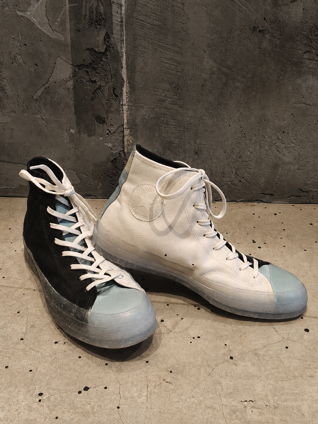 Pair of high-top sneakers with black and light blue color scheme on a concrete floor.