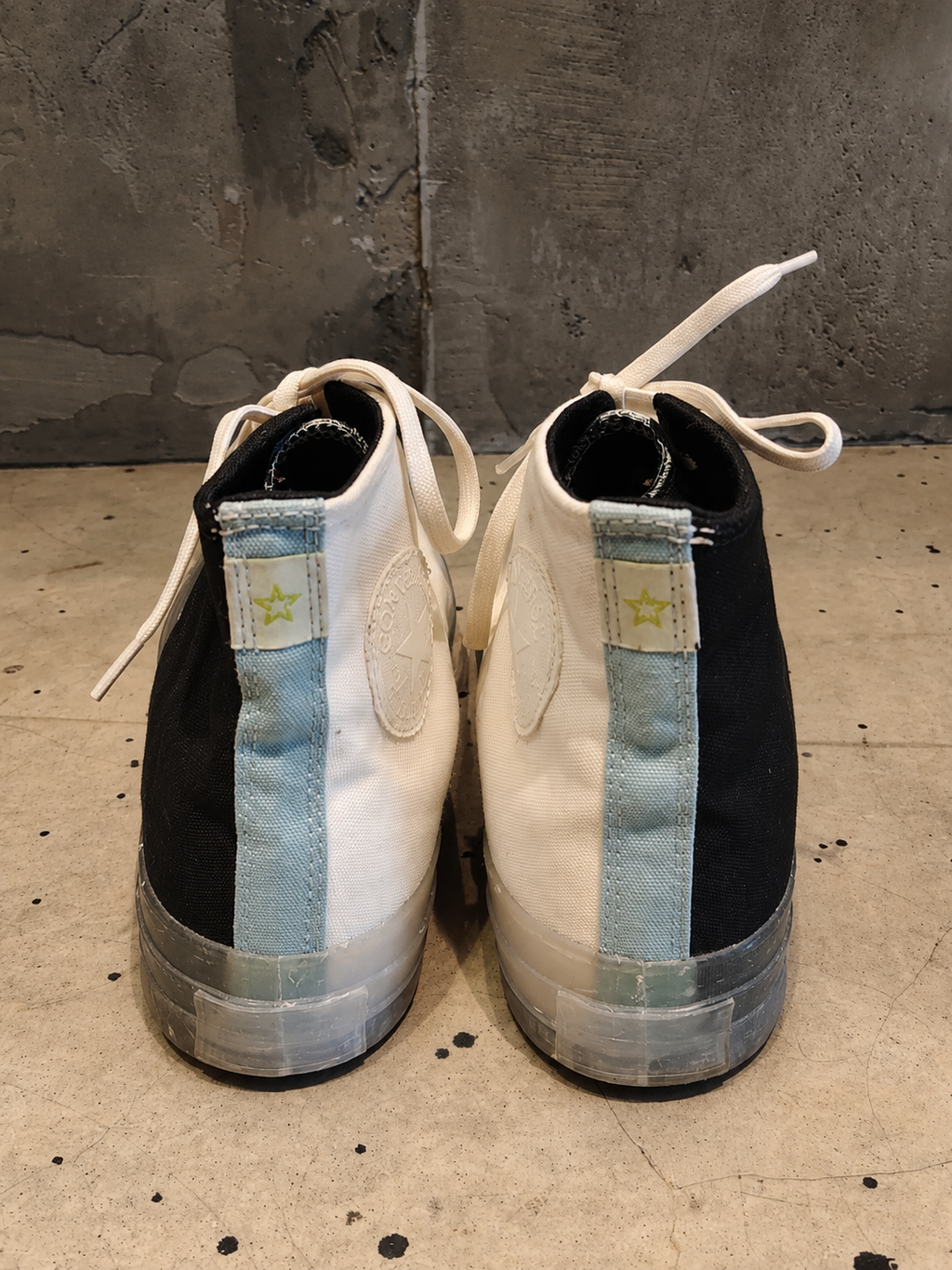 Pair of black and white sneakers with denim patches on a concrete floor.