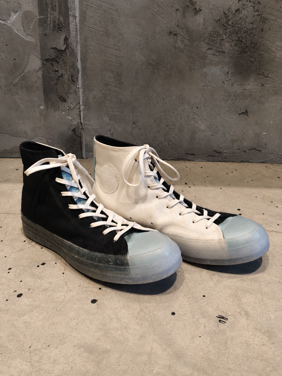 Pair of black and white high-top sneakers with blue soles on a concrete floor.