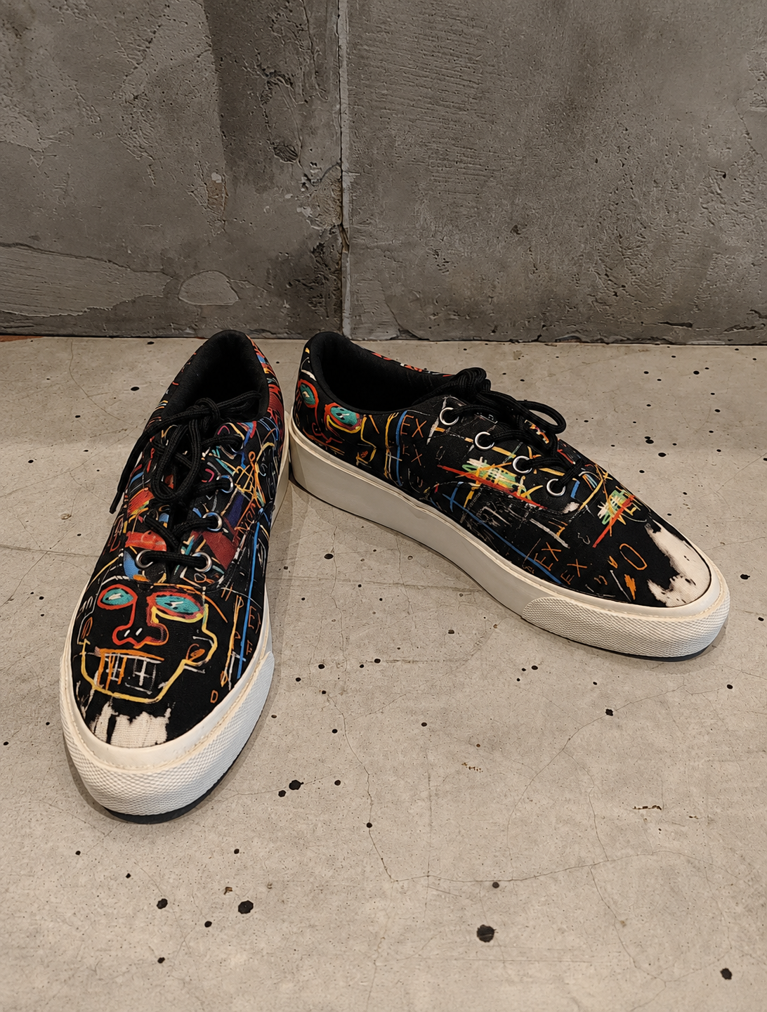 Pair of sneakers with artistic designs on a concrete floor.