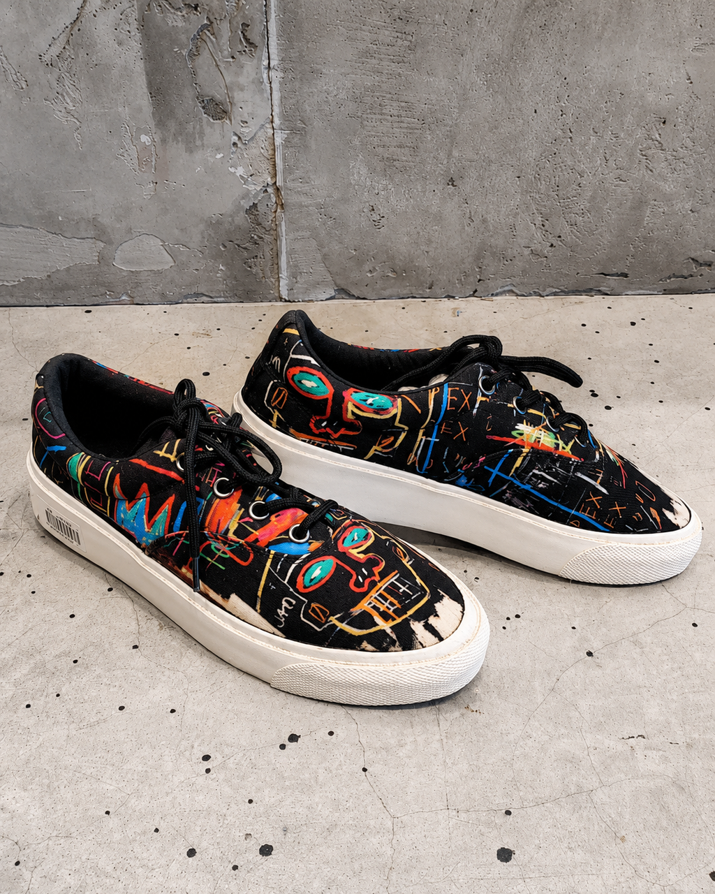 Black sneakers with colorful abstract patterns on a concrete floor.