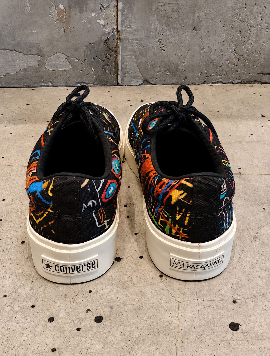 Pair of Converse sneakers with Basquiat design on a concrete floor.