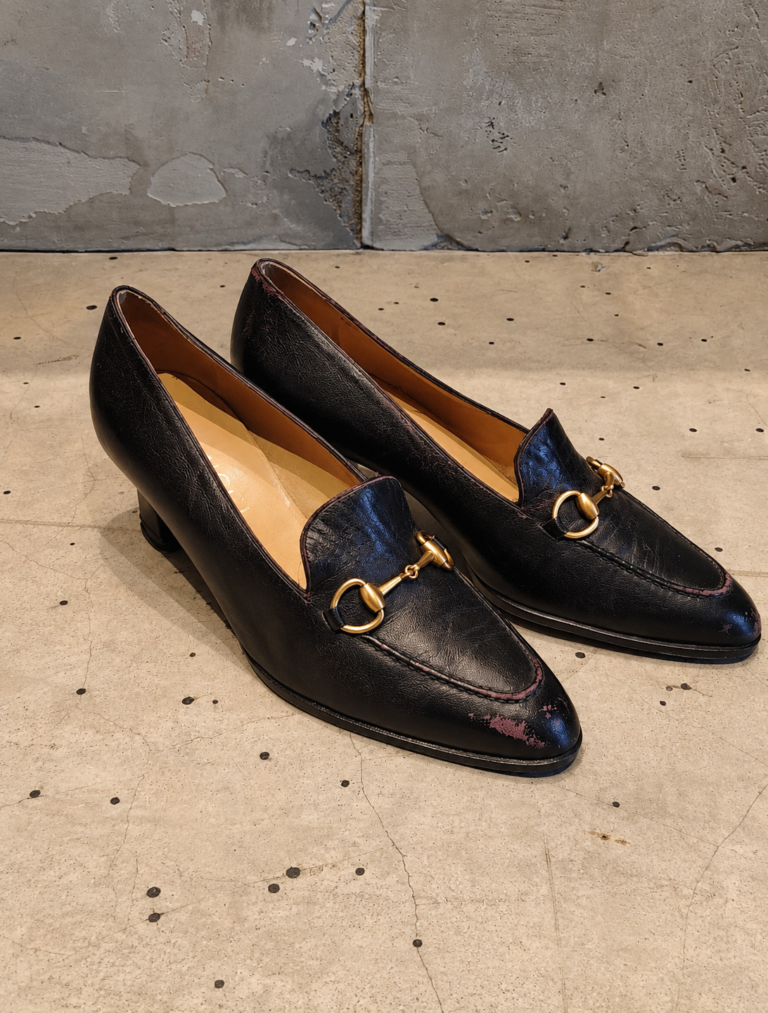Pair of black leather loafers with gold accents on a concrete floor.