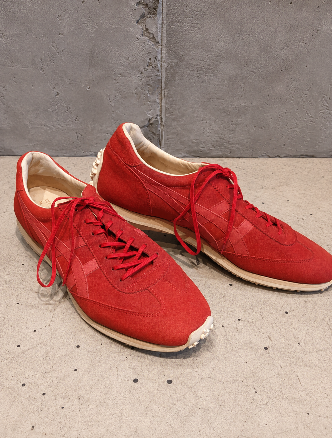 Pair of red sneakers on a concrete floor with a gray wall background