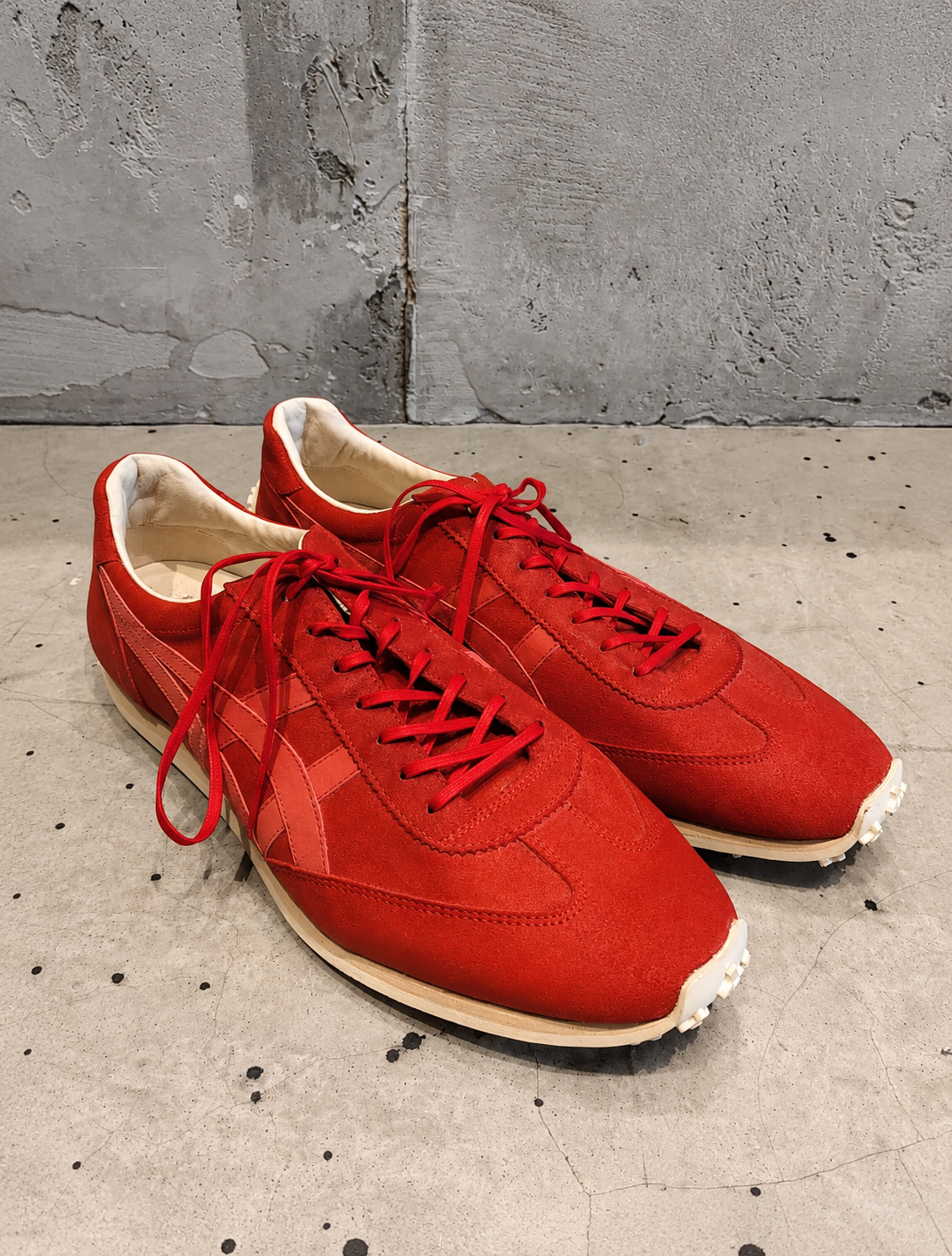 Red sneakers with white soles on a concrete floor against a gray wall.