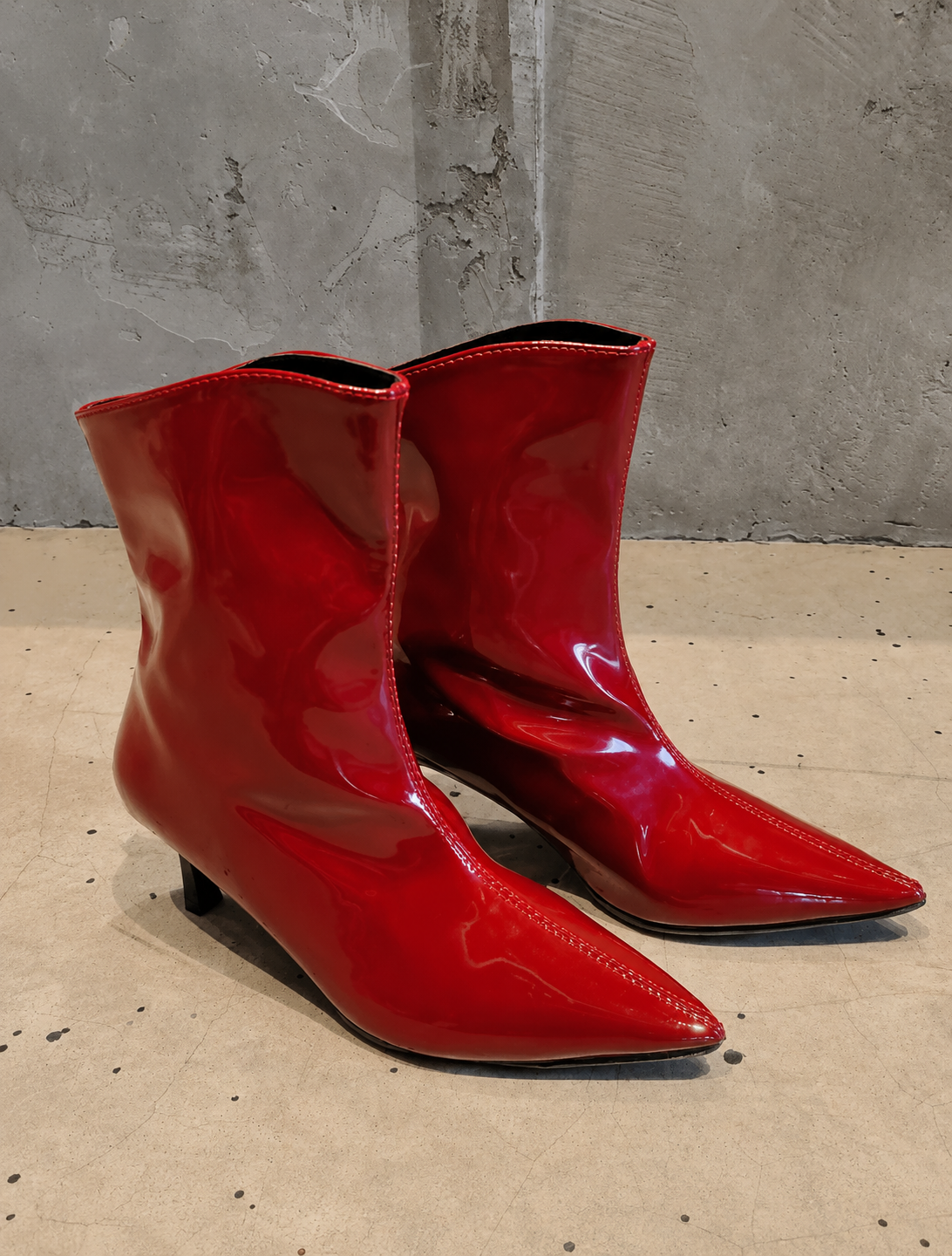 Shiny red ankle boots on a concrete floor with a gray wall background