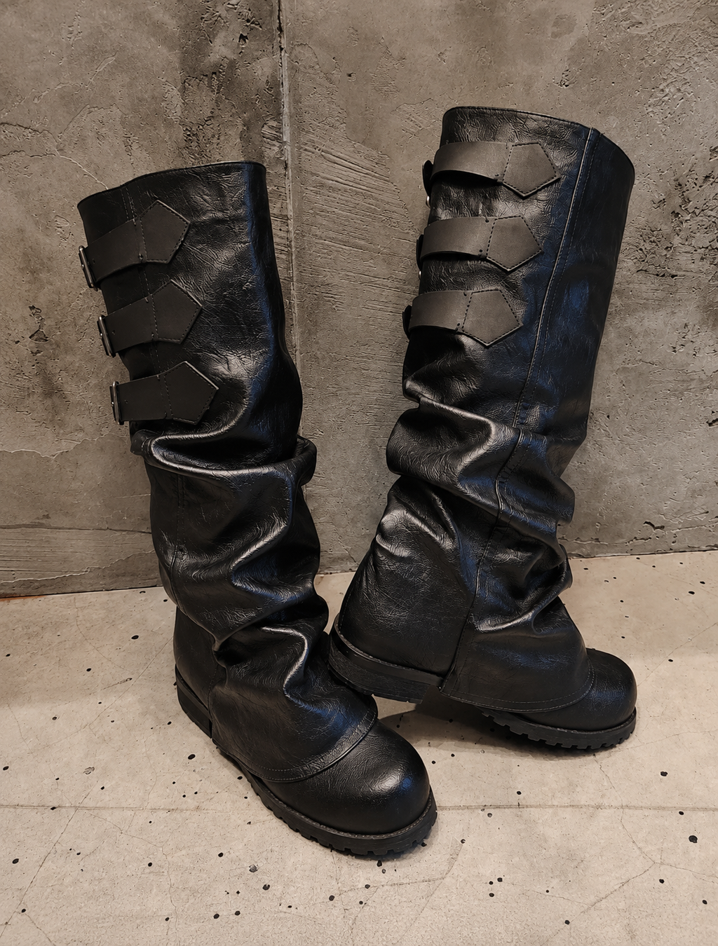 Pair of black leather boots with unique design on a textured floor and wall background