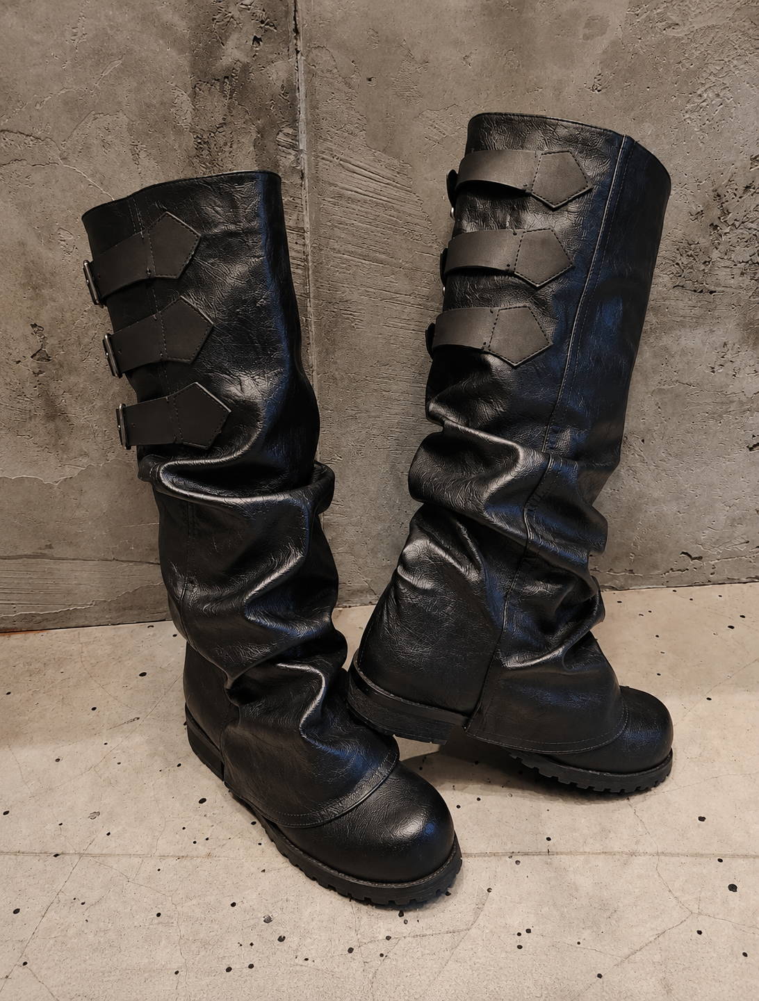 Pair of black leather boots with unique design on a textured floor and wall background