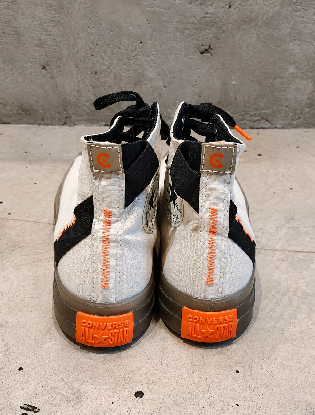 Pair of Converse All-Star sneakers with white, black, and orange design on a concrete floor.