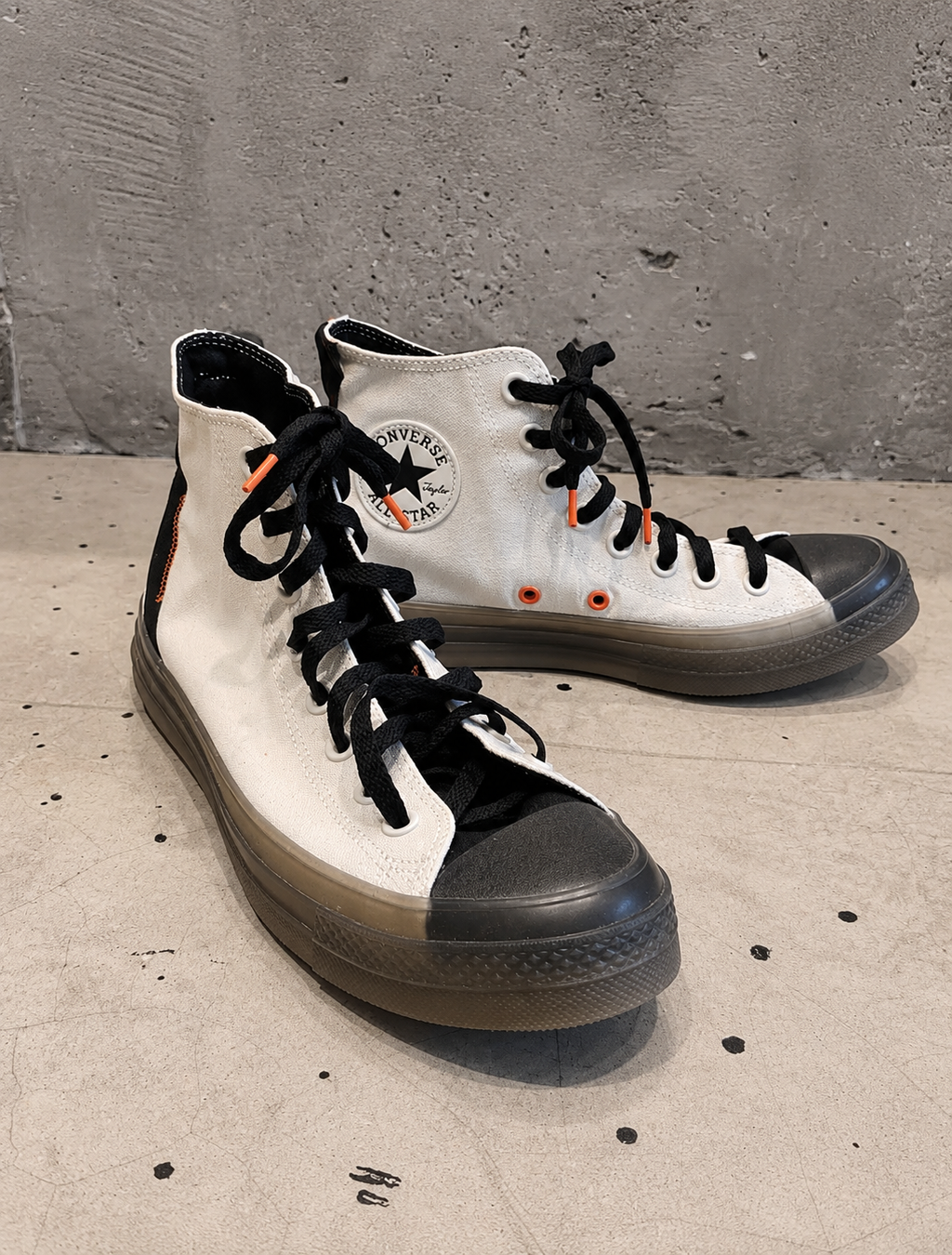 White high-top sneakers with black soles on a concrete floor.