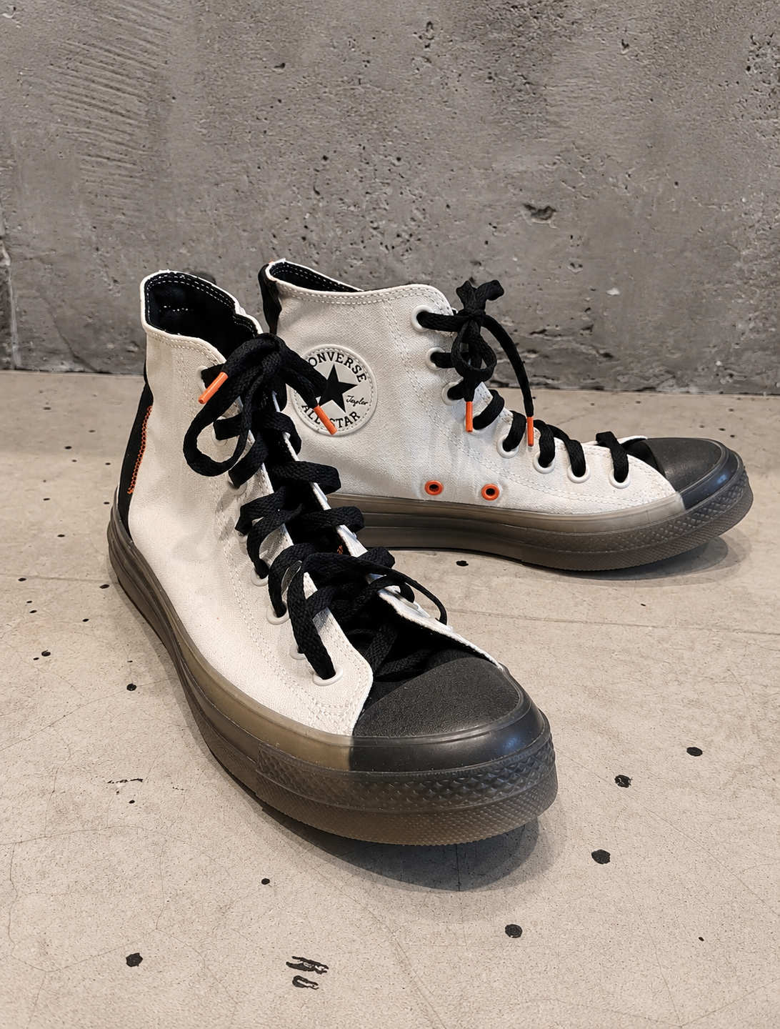 White high-top sneakers with black soles on a concrete floor.
