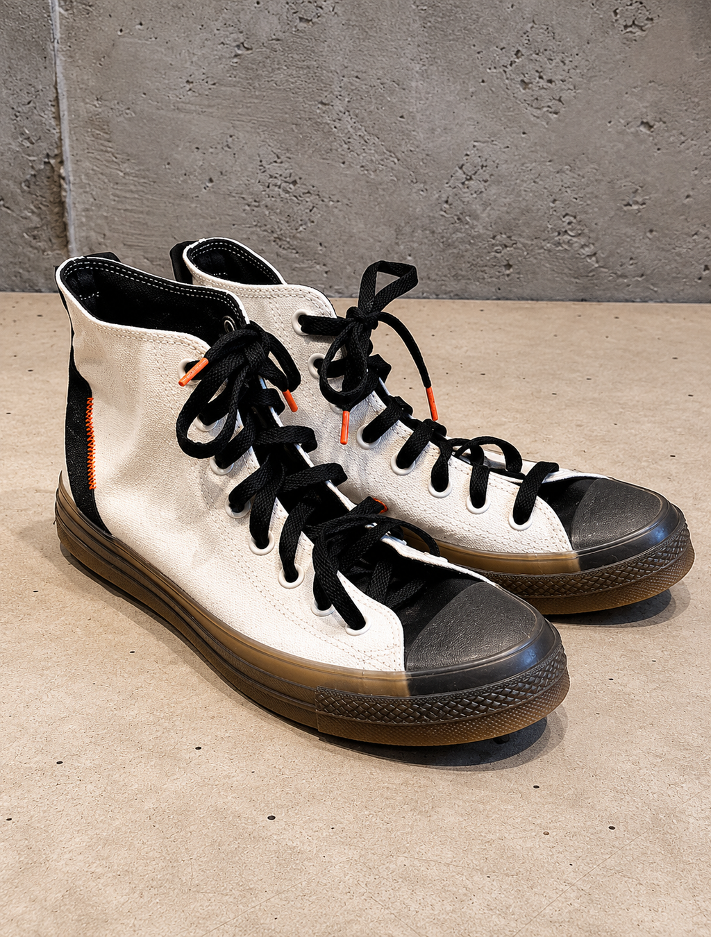Pair of white and black high-top sneakers on a concrete floor with a gray wall background.